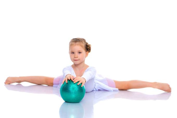 A young girl balancing on a mat with a gym ball